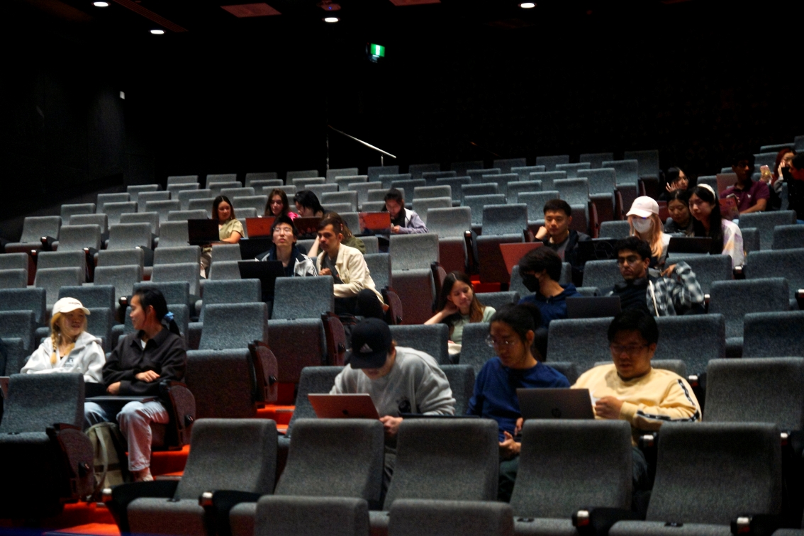 Students in a lecture hall viewing hackathon competition being presented.