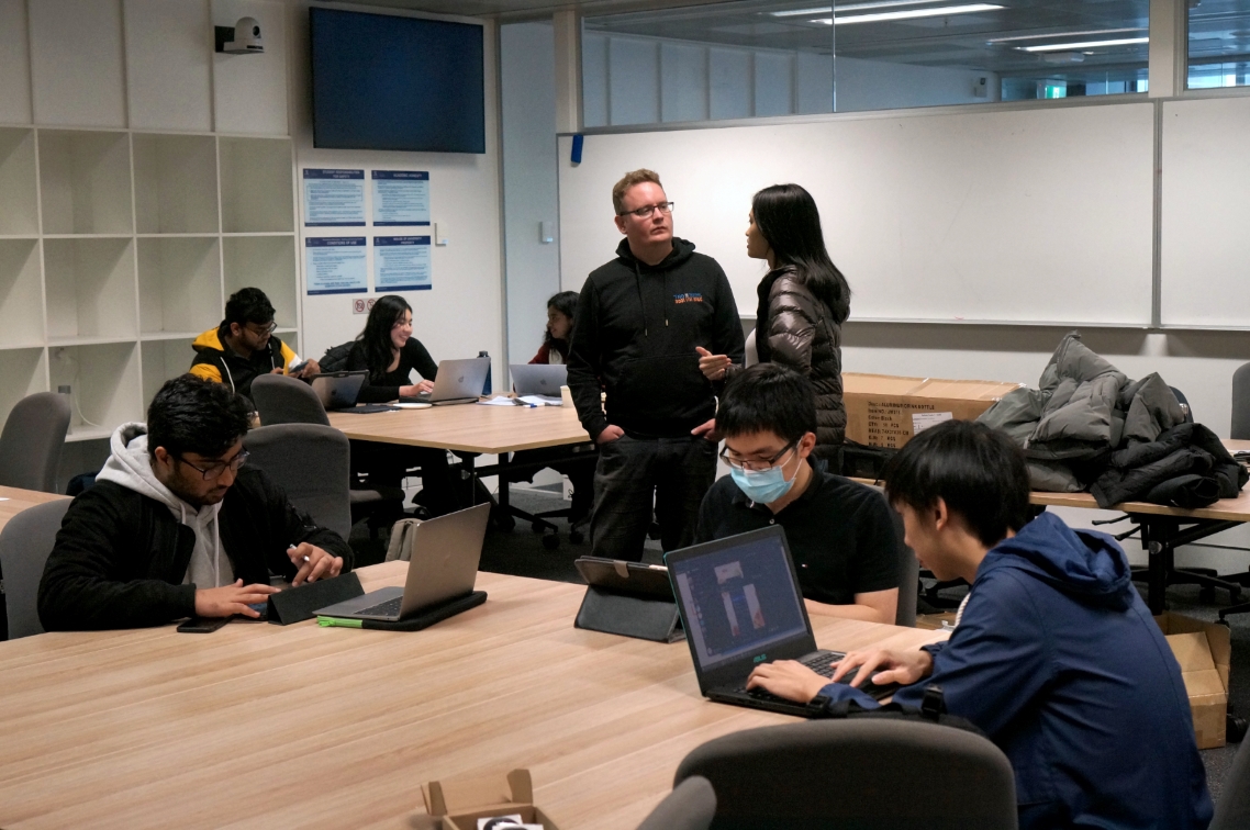 Classroom with a teacher in the middle and several students coding.